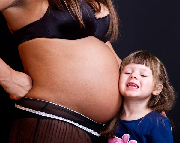 Child kissing belly of pregnant woman against black background — Stock Photo, Image