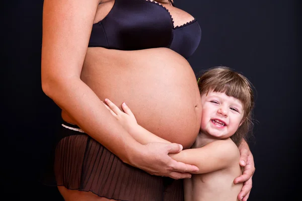 Menina criança feliz abraçando barriga da mãe grávida — Fotografia de Stock