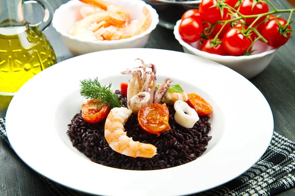 Zwarte rijst met gesneden inktvis, garnalen en tomaat op witte plaat — Stockfoto