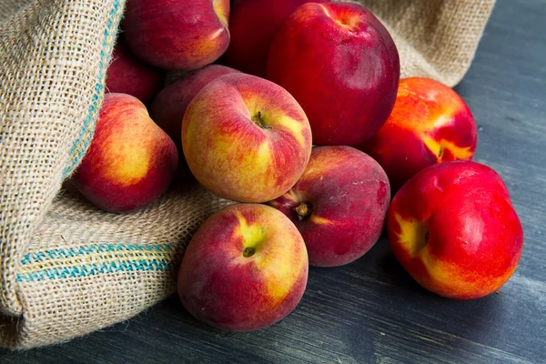 Fresh peach on burlap sack on wood — Stock Photo, Image