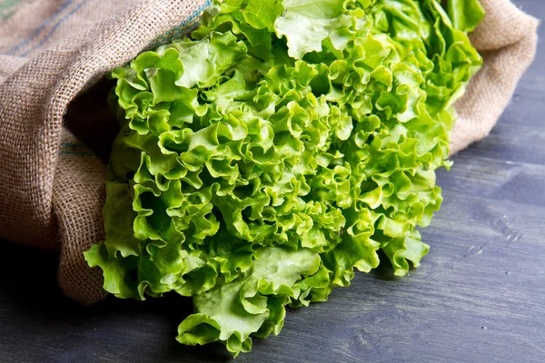 Frischer Salat im Kleesack auf Holz — Stockfoto