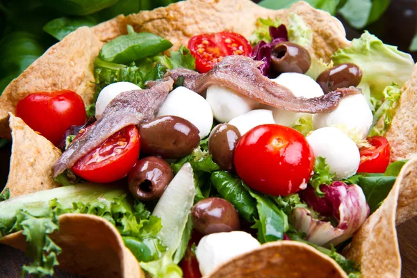 Ensalada mixta con mozzarella y anchoa en una cesta de pan —  Fotos de Stock