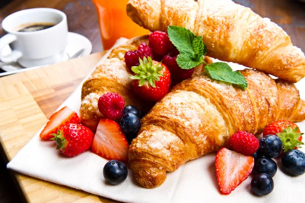 Fresh tasty croissants with berries on wooden background — Stock Photo, Image