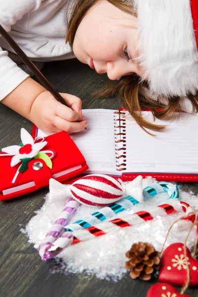 Funny girl in Santa hat writes letter to Santa near christmas de — Stock Photo, Image