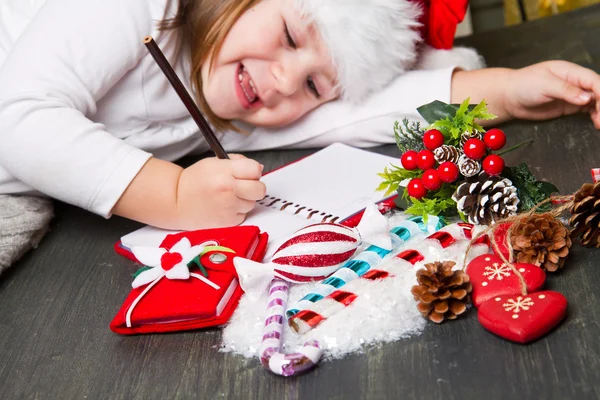 Funny girl in Santa hat writes letter to Santa near christmas de — Stock Photo, Image