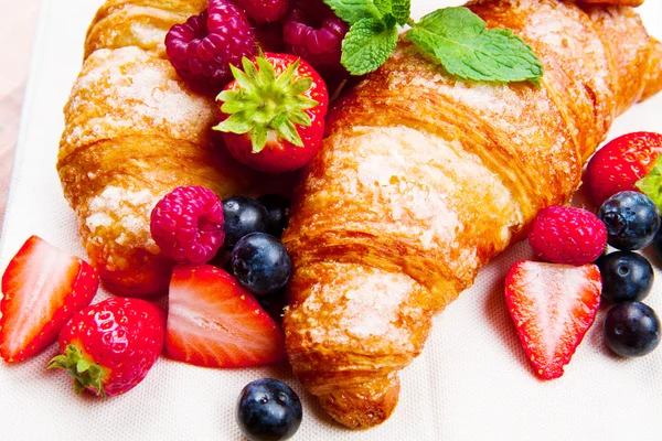 Fresh tasty croissants with berries on wooden background — Stock Photo, Image