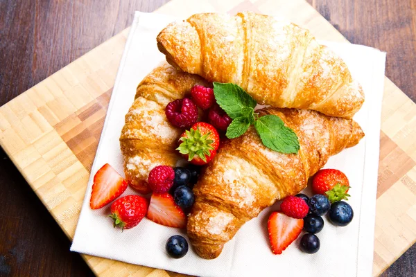 Fresh tasty croissants with berries on wooden background — Stock Photo, Image