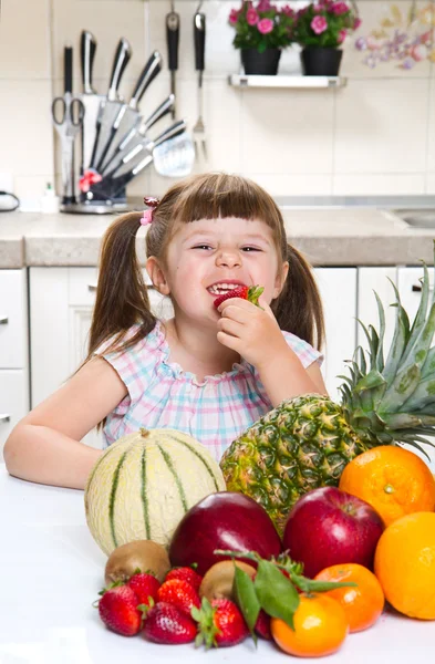 Pequeña linda chica sosteniendo y comiendo una fresa en la cocina — Foto de Stock
