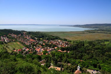 Yükseltilmiş bir perspektif, yemyeşil ağaçlar ve Macaristan 'da sakin bir göl ile çevrili kırmızı kiremitli çatıların yer aldığı pitoresk bir köy yakalıyor.