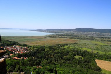 Yükseltilmiş bir perspektif, yemyeşil ağaçlar ve Macaristan 'da sakin bir göl ile çevrili kırmızı kiremitli çatıların yer aldığı pitoresk bir köy yakalıyor.