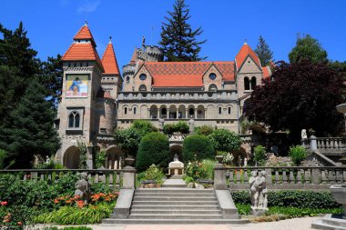 Süslü, kırmızı çatıları olan çok taretli bir bina, Macaristan 'da heykel ve canlı çiçeklerin yer aldığı süslü teraslı bahçelerin arkasında duruyor.
