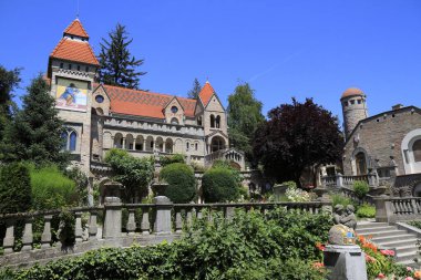 Süslü, kırmızı çatıları olan çok taretli bir bina, Macaristan 'da heykel ve canlı çiçeklerin yer aldığı süslü teraslı bahçelerin arkasında duruyor.