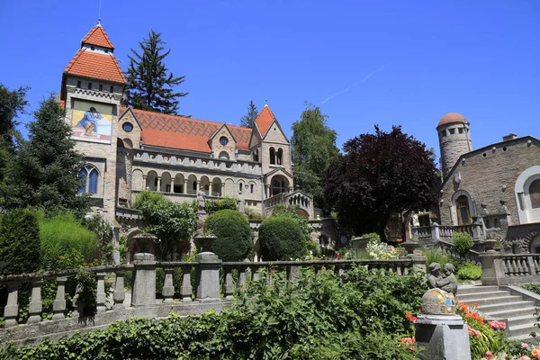 Süslü, kırmızı çatıları olan çok taretli bir bina, Macaristan 'da heykel ve canlı çiçeklerin yer aldığı süslü teraslı bahçelerin arkasında duruyor.