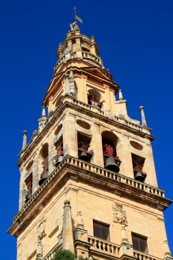 Cordoba 'nın Mezquita-Katedrali' nin antik çan kulesi canlı mavi gökyüzüne karşı yükselir, yıpranmış taşlar, kemerli çan odaları ve geleneksel bronz çanlar sergilenir..