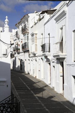 Tarihsel beyazlatılmış atari salonu bir çan kulesi ve parlak mavi gökyüzünün altındaki demir kapıyla süslü taş bir kapı çerçevesi, Vejer de la Frontera, İspanya