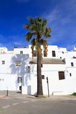 Tarihsel beyazlatılmış atari salonu bir çan kulesi ve parlak mavi gökyüzünün altındaki demir kapıyla süslü taş bir kapı çerçevesi, Vejer de la Frontera, İspanya