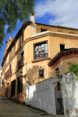 Tarihsel beyazlatılmış atari salonu bir çan kulesi ve parlak mavi gökyüzü altında demirden bir kapısı olan süslü taş bir portal, Ronda, İspanya