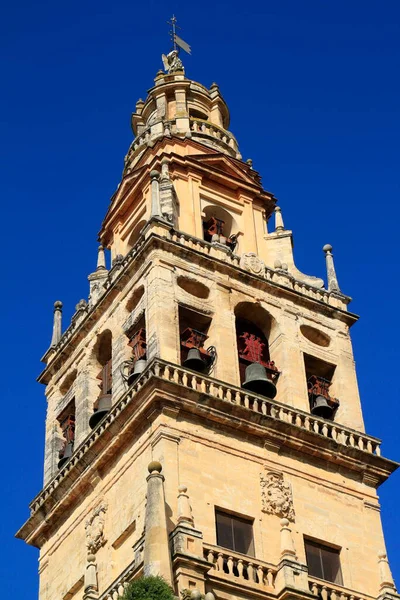 Cordoba 'nın Mezquita-Katedrali' nin antik çan kulesi canlı mavi gökyüzüne karşı yükselir, yıpranmış taşlar, kemerli çan odaları ve geleneksel bronz çanlar sergilenir..