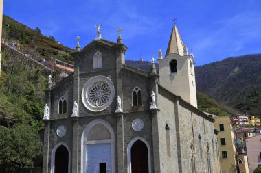 Uzun çan kulesi, kemerli kapı aralığı olan tarihi bir kilise cephesi.