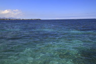Canlı turkuaz okyanus dalgalanan bulutların dramatik gökyüzünün altında uzak bir tropikal kıyıya uzanıyor.
