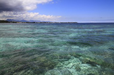 Canlı turkuaz okyanus dalgalanan bulutların dramatik gökyüzünün altında uzak bir tropikal kıyıya uzanıyor.