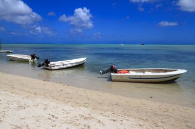 Sürat tekneleri şeffaf, sakin bir okyanus suyuna demirlemiş kumlu bir sahile yakın.