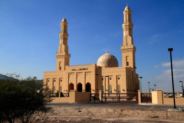 İki uzun minarenin ve süslü bir kubbenin yer aldığı büyük, kumlu bir cami canlı mavi bir gökyüzüne karşı duruyor..