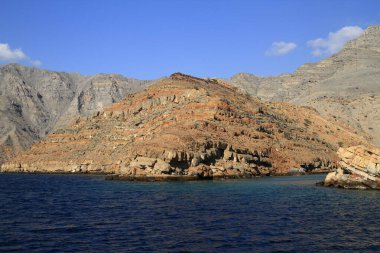 Çorak, görkemli bir sıradağ görünür jeolojik katmanlarıyla berrak bir günde sakin, derin mavi okyanusun üzerinde duruyor..