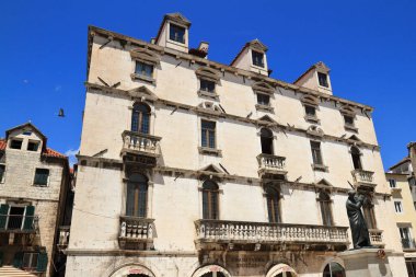 Güneşli bir günde pek çok pencere ve balkona sahip tarihi taş binalar, klasik Avrupa mimarisinin sergilendiği dar bir cadde..