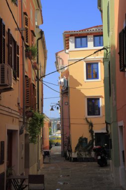 Eski bir Akdeniz kasabasındaki sessiz, renkli dar bir sokak pastel binalar, ahşap panjurlar ve kaldırımlarla kaplı, büyüleyici, kırsal ve güneşten ısınmış bir seyahat atmosferini çağrıştırıyor..