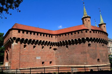 Güneşli bir günde mavi gökyüzünün altında gururla duran etkileyici kuleleri ve kırmızı kiremitli çatısı olan görkemli antik bir tuğla kale duvarı..