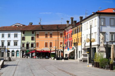 Parlak renkli binalar, kafeler ve açık mavi gökyüzü altında yayalar olan hareketli tarihi Avrupa şehir meydanı.