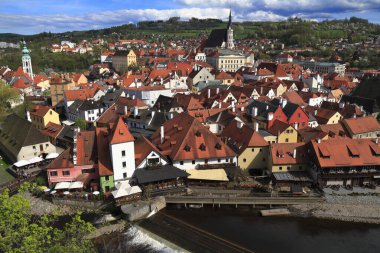 Cesky Krumlovs 'un panoramik manzarası yoğun kırmızı kiremit çatıları, nehir kenarındaki restoranlar, önemli kilise kulesi ve yeşil tepeler, Avrupa cazibesini, turizmini aktaran