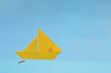 Kavramsal Sarı Kağıt Tekne ve Mavi Arkaplanda Minyatür İnsanlar