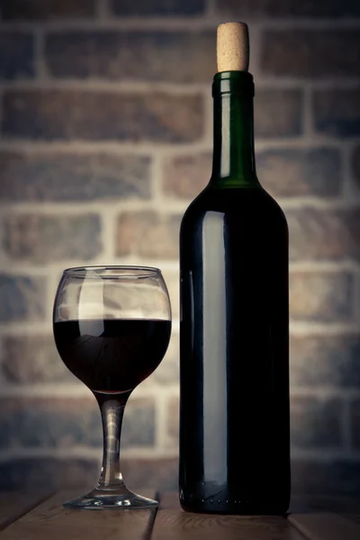 Láhev vína a skla na dřevěný stůl s cihly zdi backgro — Stock fotografie