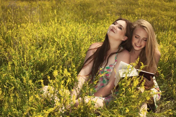 Dwie piękne dziewczyny uśmiechający się czytając książkę przed latem Park. — Zdjęcie stockowe