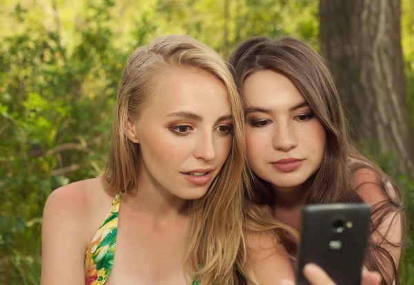 Meninas jovens olham para a tela do telefone ao ar livre loira e brune — Fotografia de Stock