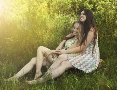Çim ve gülümseme üzerinde siting iki mutlu arkadaş genç kadın
