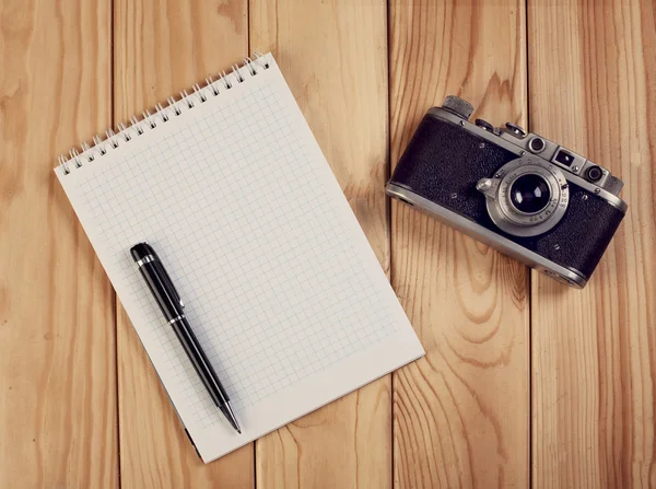 Cuaderno con pluma y cámara vintage en escritorio de madera. Vista superior . —  Fotos de Stock