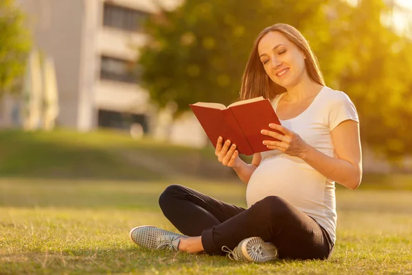 Une femme enceinte lit un livre sur un champ vert — Photo