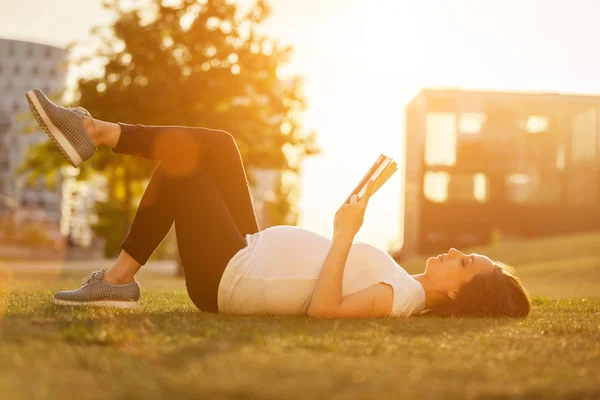 Pregnant woman is reading a book on a green field — Stock Photo, Image