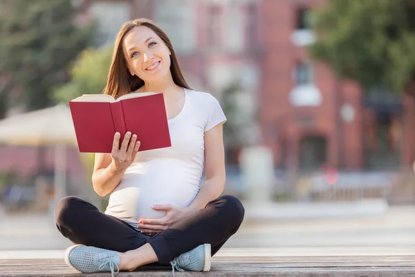 Mujer embarazada leyendo el libro en un banco — Foto de Stock
