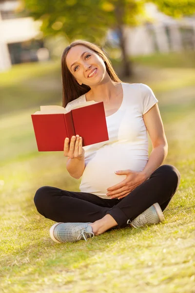 Mujer embarazada leyendo un libro en un campo verde — Foto de Stock