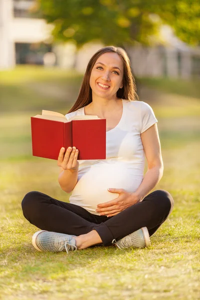 Femme enceinte lisant un livre sur un champ vert — Photo