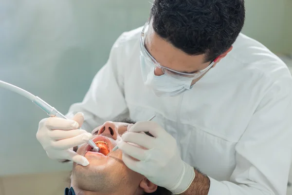 Dentista fazendo um tratamento higiênico para um paciente de 40 anos vendido — Fotografia de Stock