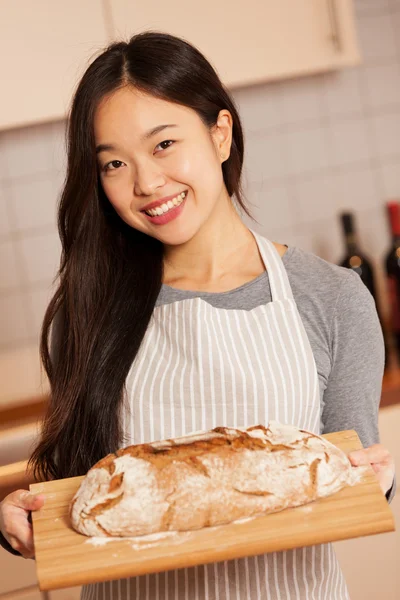 Sorrindo mulher asiática está segurando pão fresco assado em um tra de madeira — Fotografia de Stock