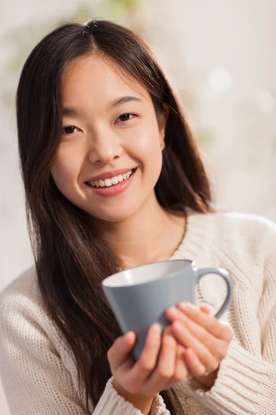 Asiatin mit heißem Becher in den Händen lächelt in die Kamera — Stockfoto