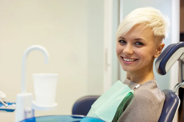 Loira sorrindo mulher sentada no dentista e olhando para — Fotografia de Stock