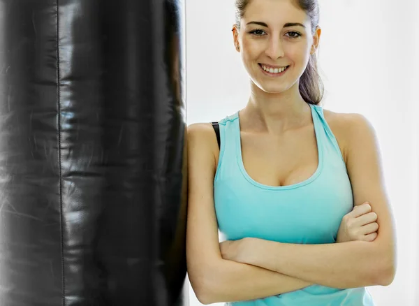 Joven morena sonriente está de pie junto a un saco de boxeo —  Fotos de Stock