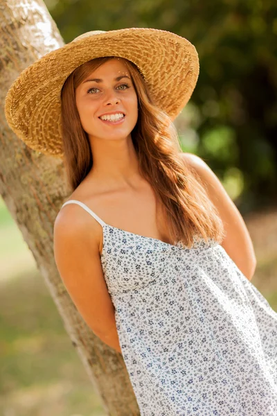 Belle fille souriante avec chapeau derrière un arbre — Photo